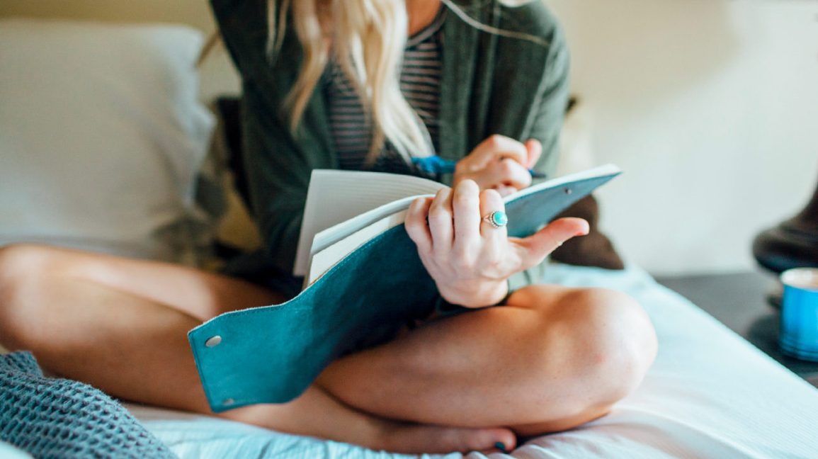 A girl writing diary while sitting on the bed